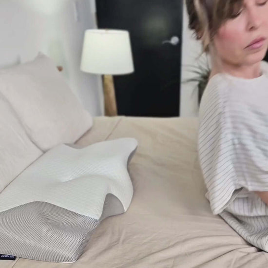No.1 Comfort! CloudNest™ Premium Relief Pillow on a bed next to a woman preparing to sit down.